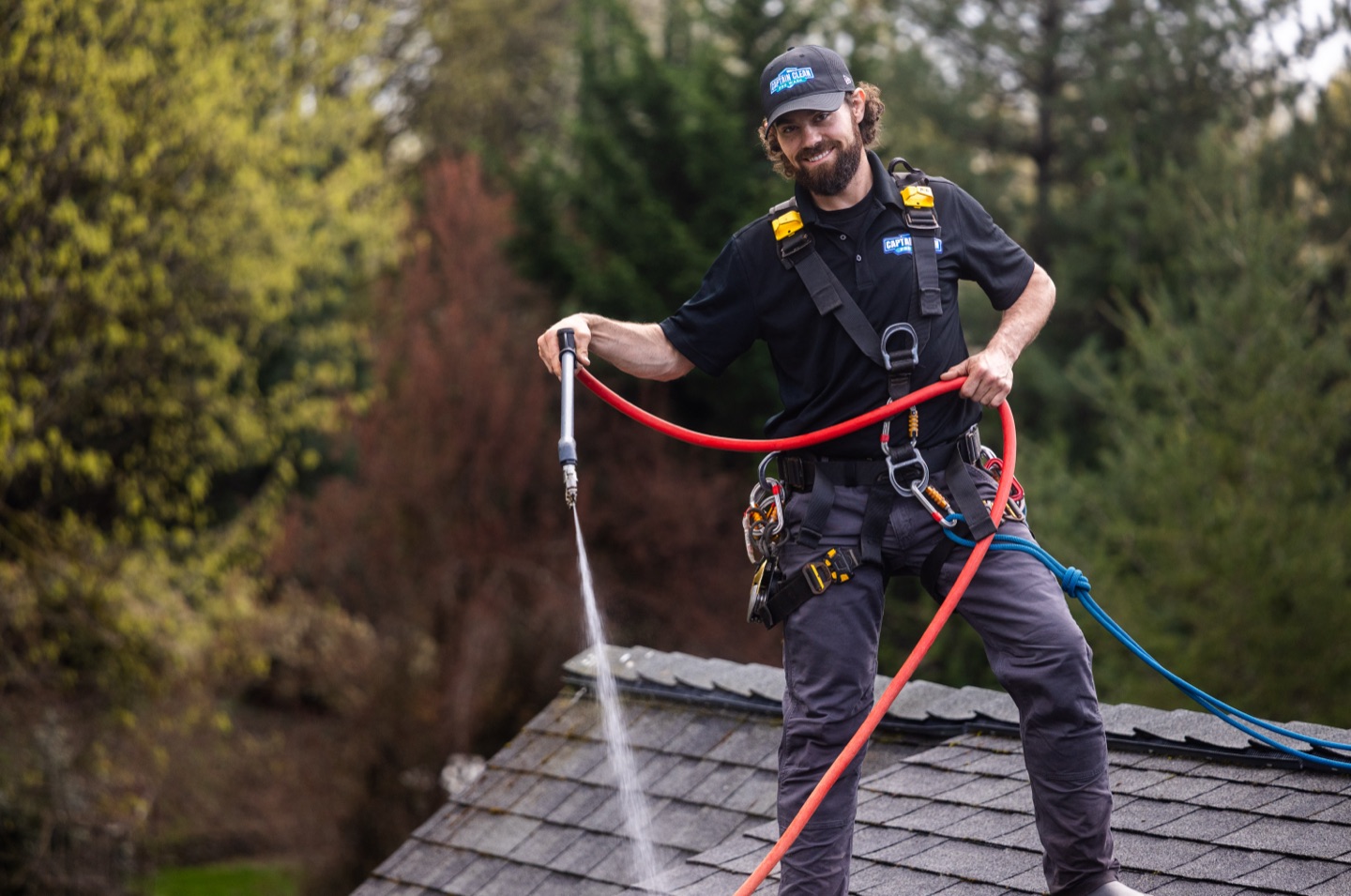 Technician in a safety harness pressure-washing a roof