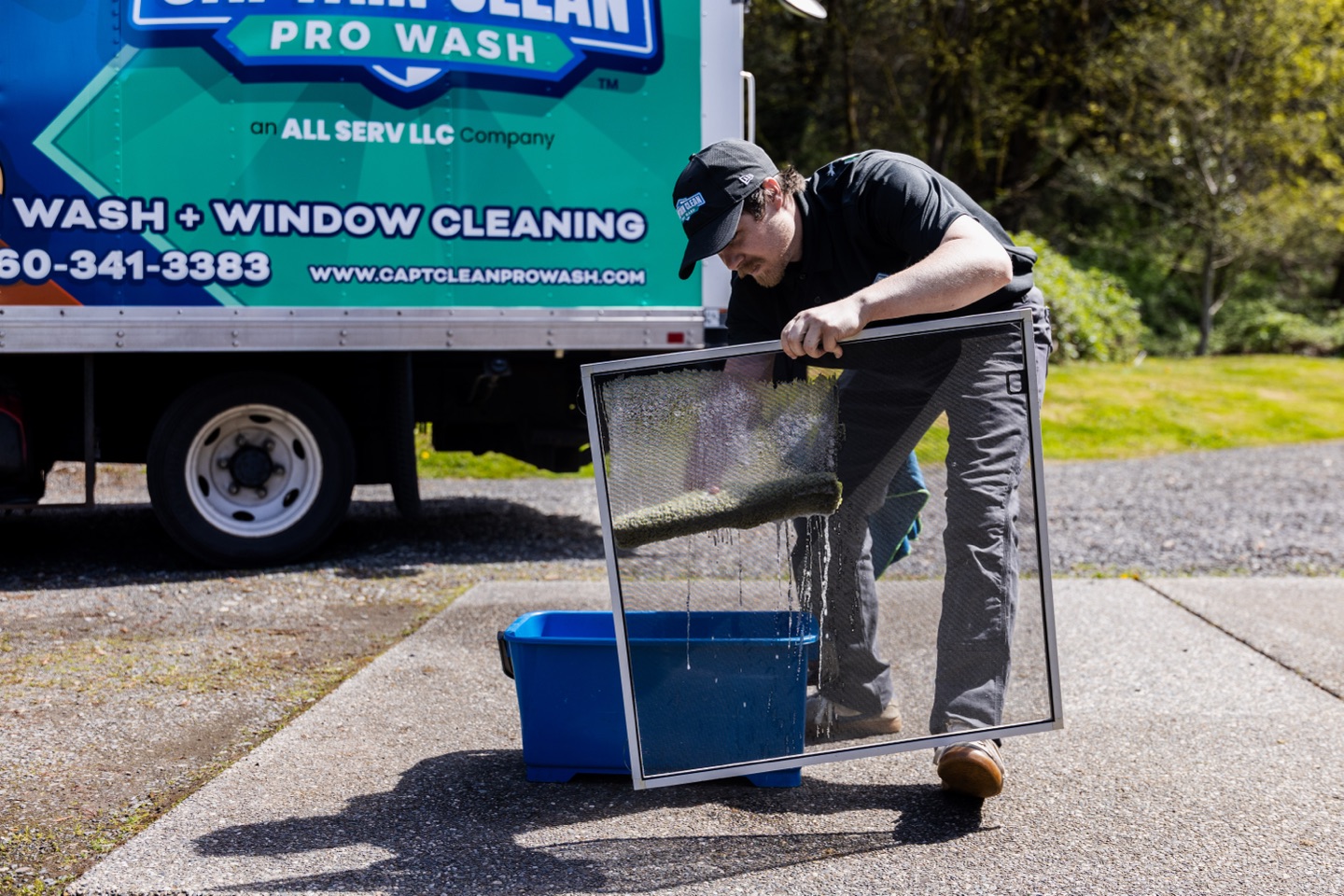 Technician scrubbing a window screen beside the branded truck