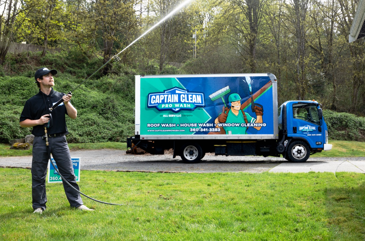 Technician sending a high spray arc across the yard, the Captain Clean Pro Wash truck behind him