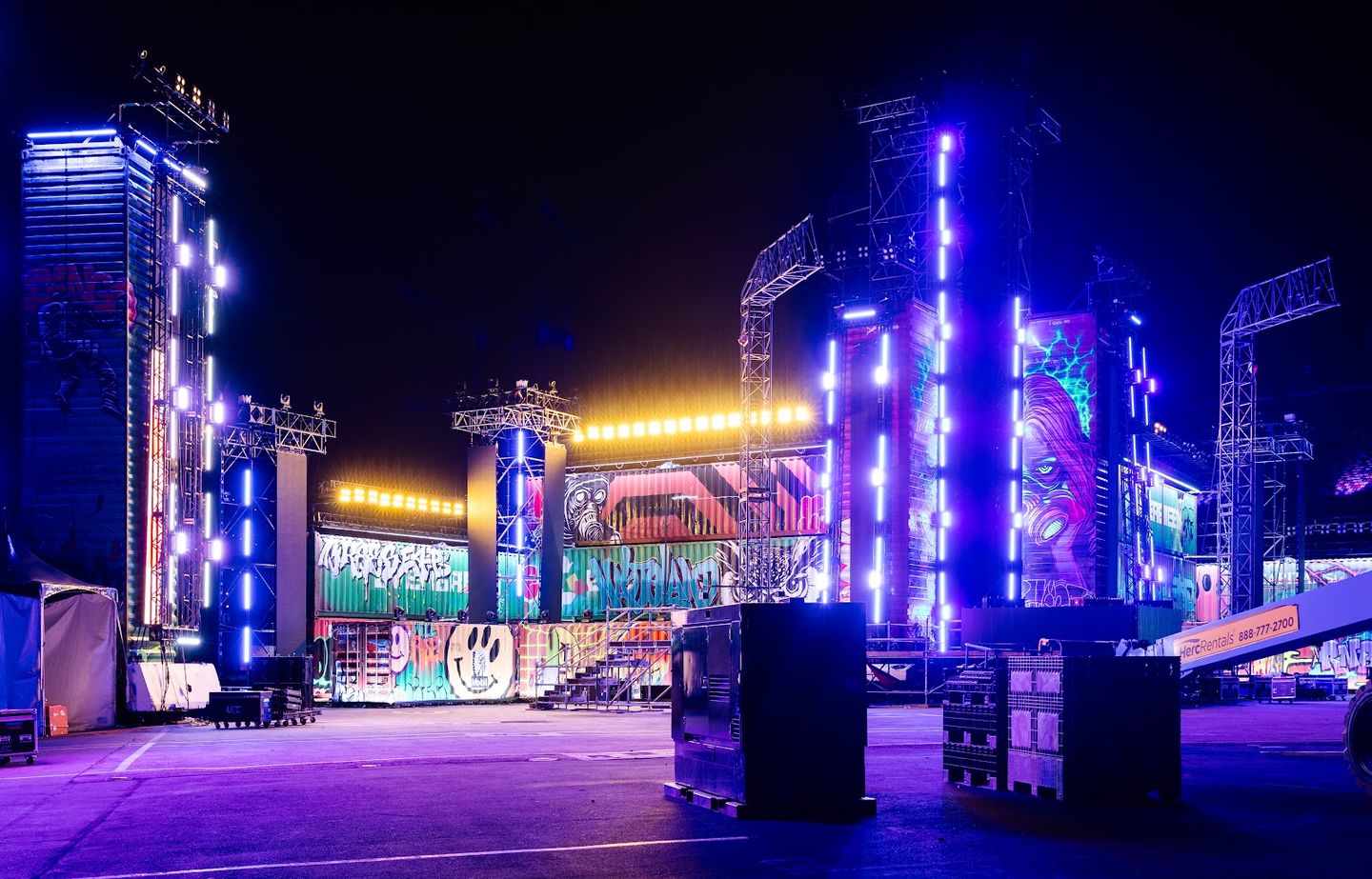 A stage built from painted shipping containers, lit purple and gold at night