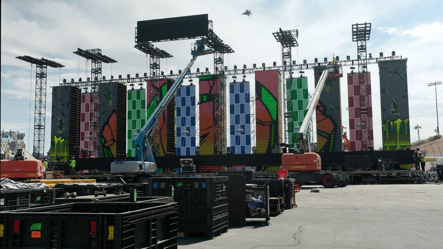 Boom lifts at a stage wall of painted panels while the crew builds it