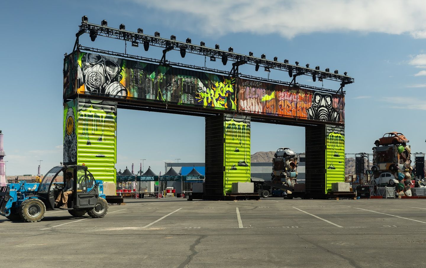 A painted container gateway under a lighting truss, a telehandler driving past during the build