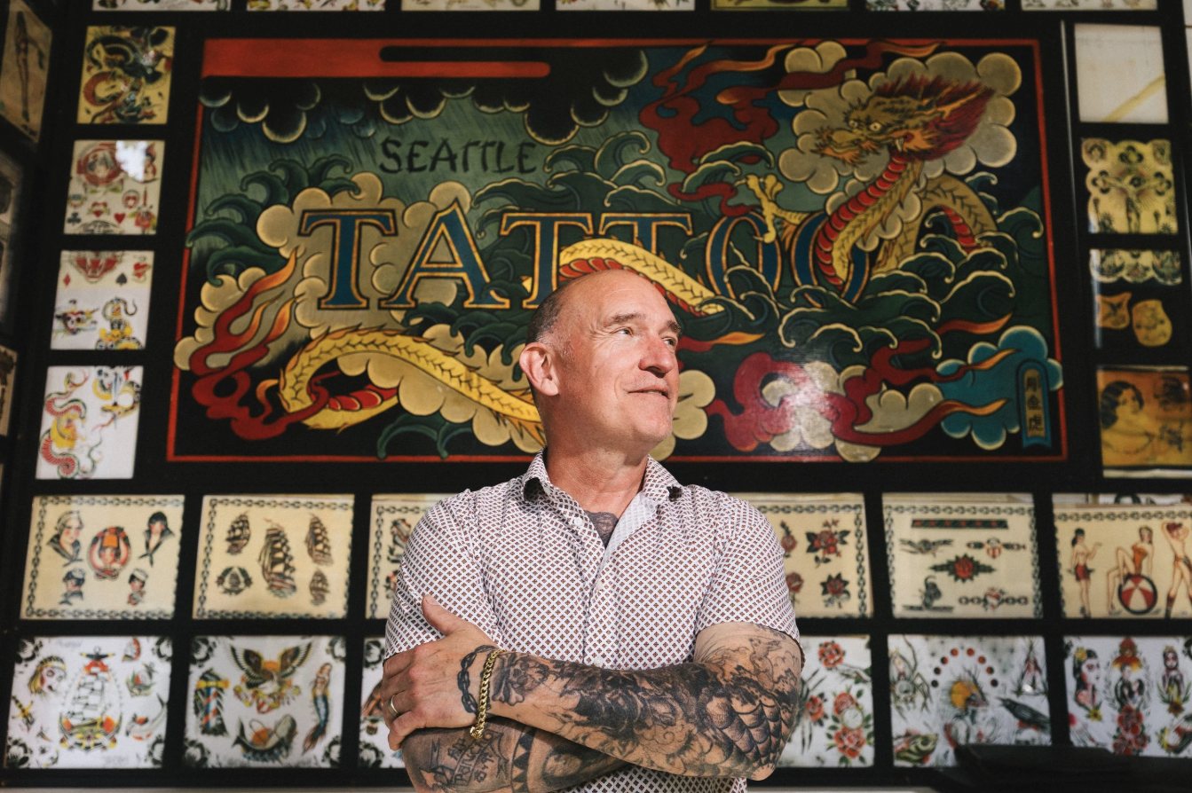 Owner in front of the shop's hand-painted flash wall